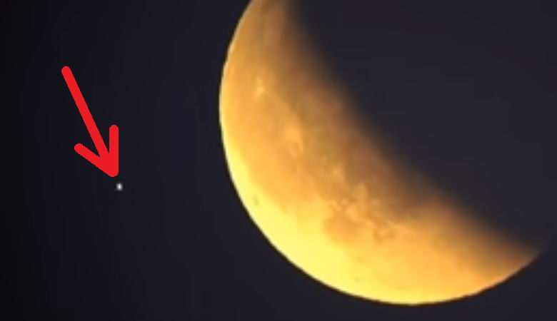 Um OVNI piscando voando contra uma lua vermelha